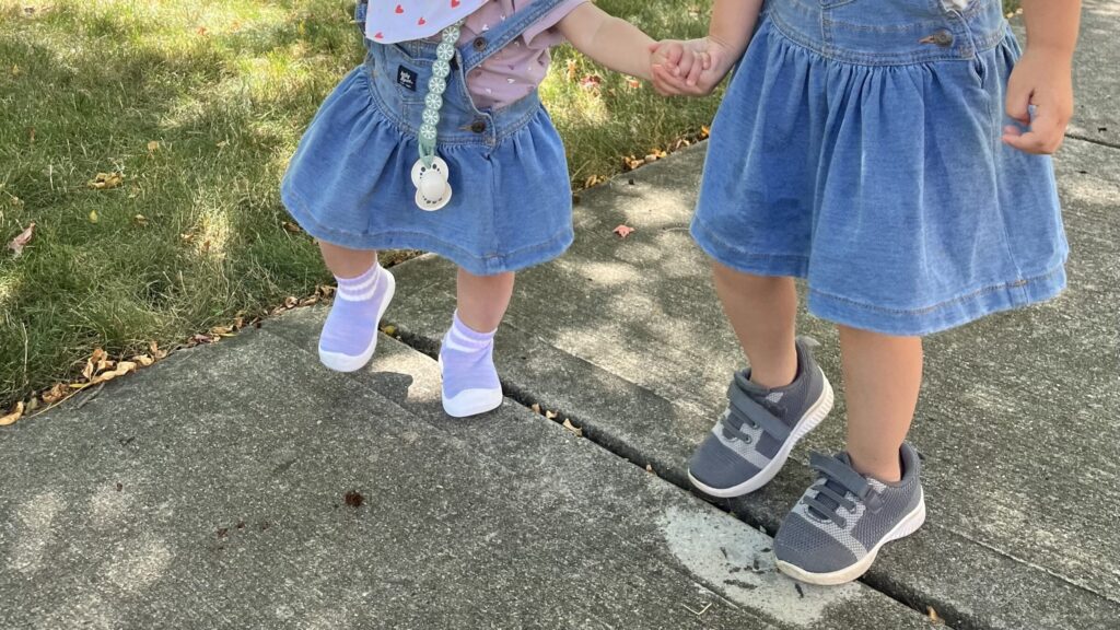 3歳と1歳が手を繋いで歩いている様子を撮影した写真